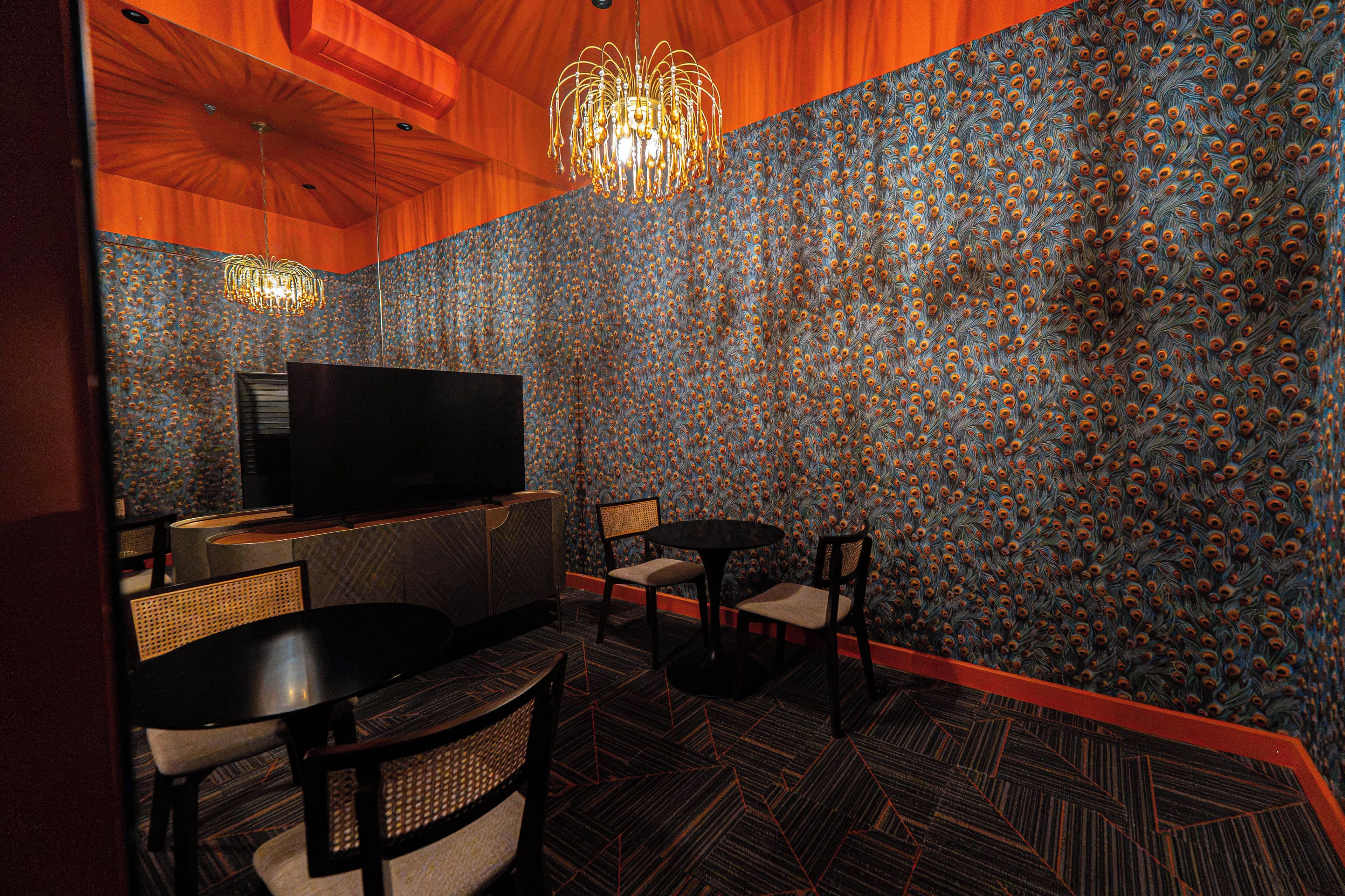 A room with a television, two chairs, a table, and a patterned wall.