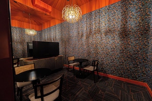 A room with a television, two chairs, a table, and a patterned wall.