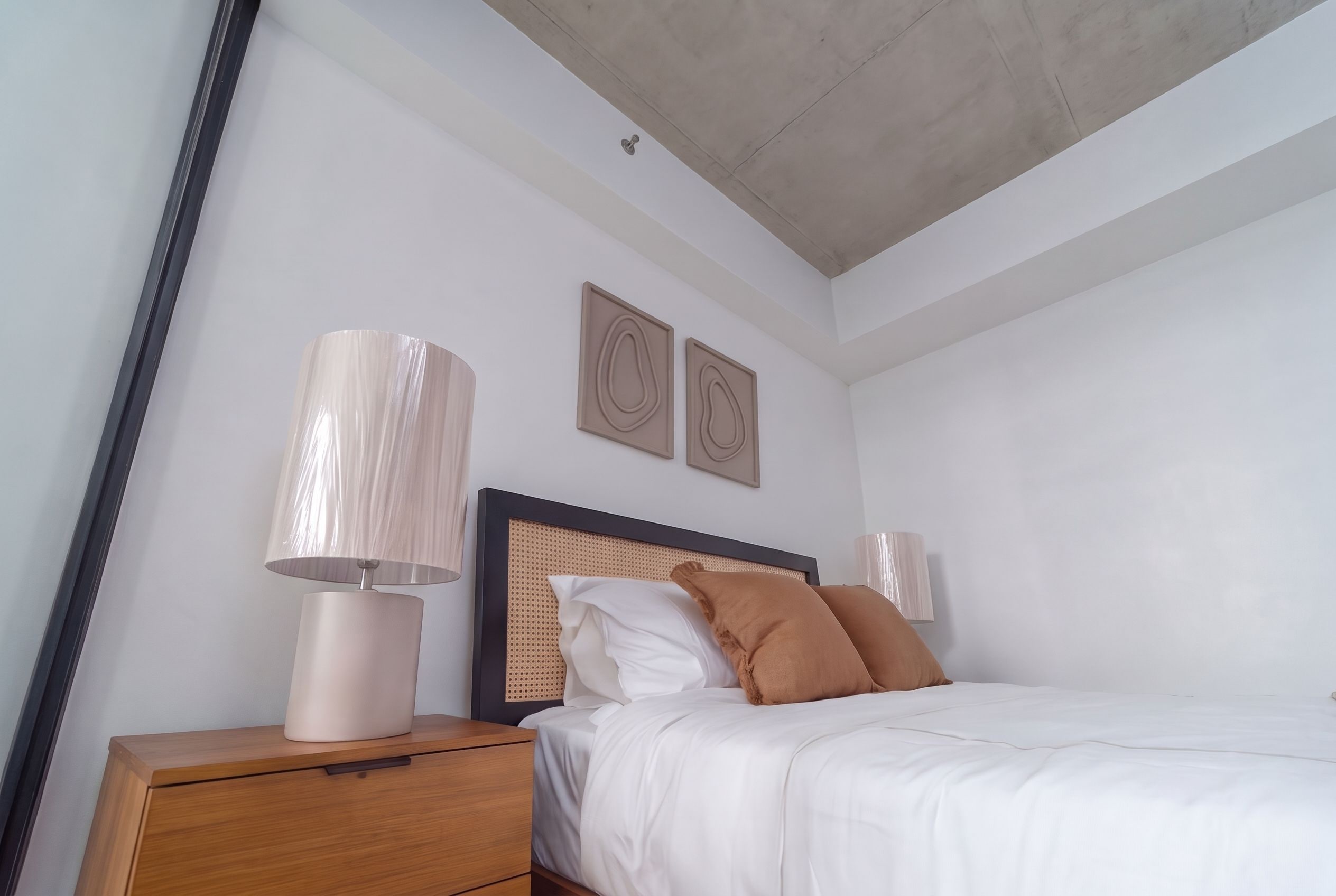Un dormitorio con cama, mesita de noche, lámpara y dos cuadros en la pared.