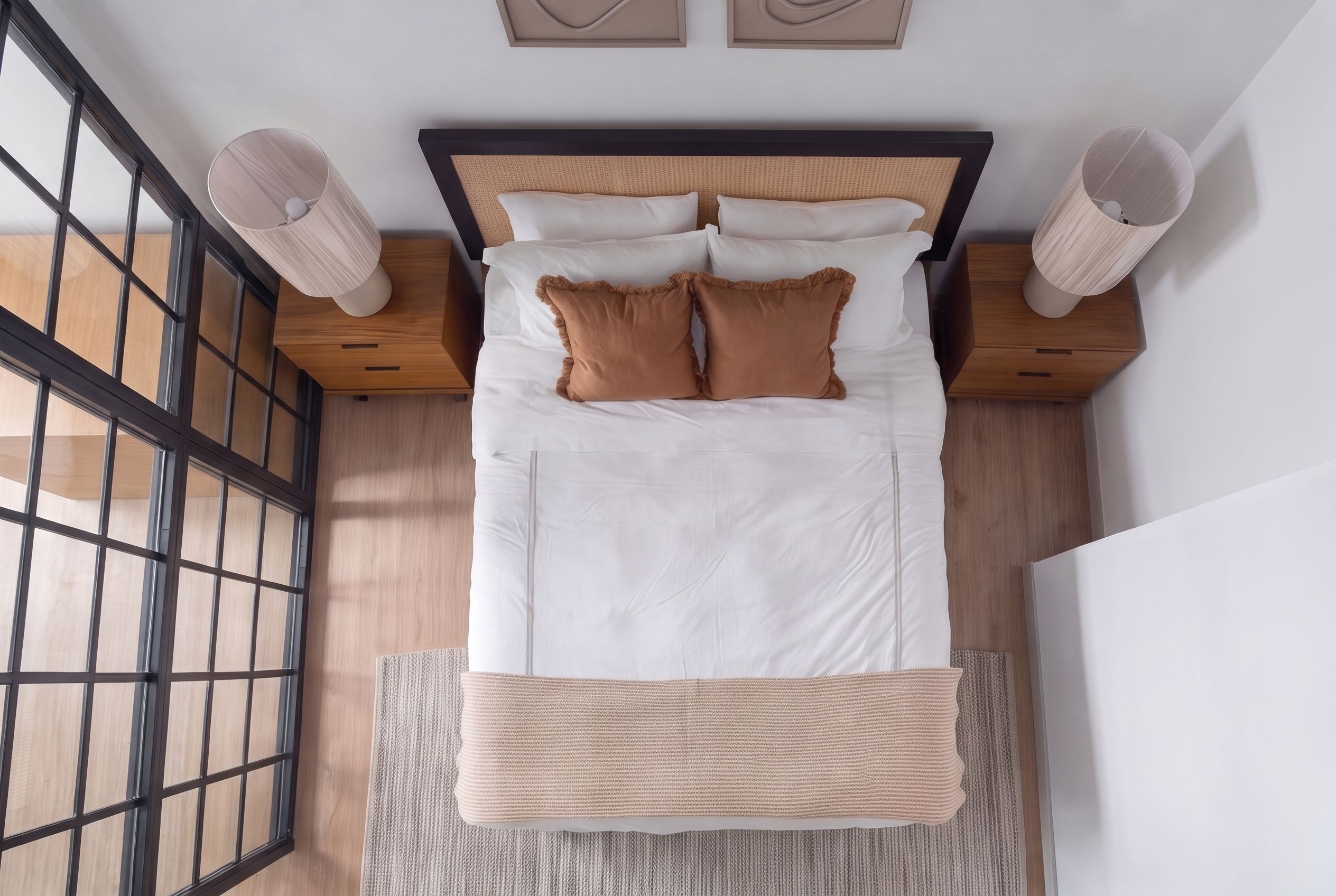 Un lit bien fait, avec du linge de lit blanc et deux oreillers marron, une tête de lit en bois et un tapis tissé au pied du lit.