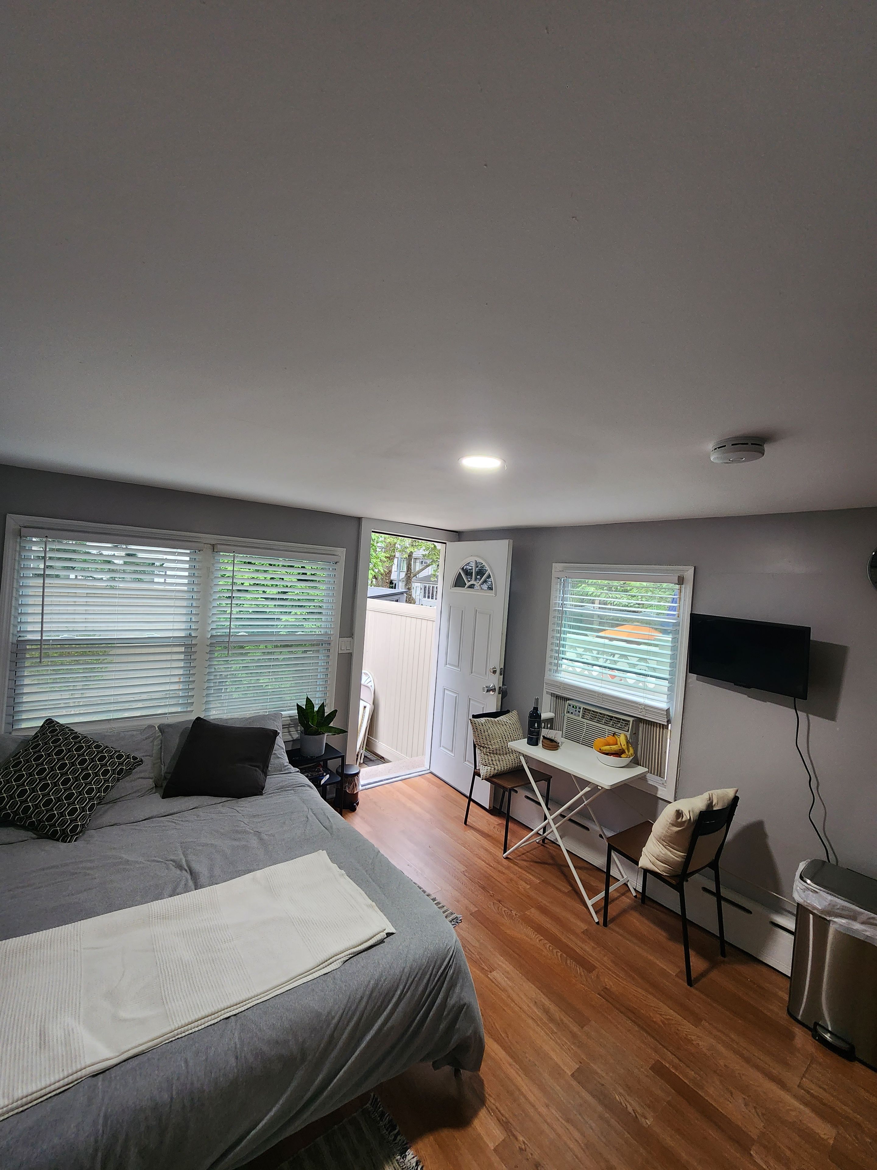A bedroom with a bed, a desk, a chair, a TV, and a window with blinds.
