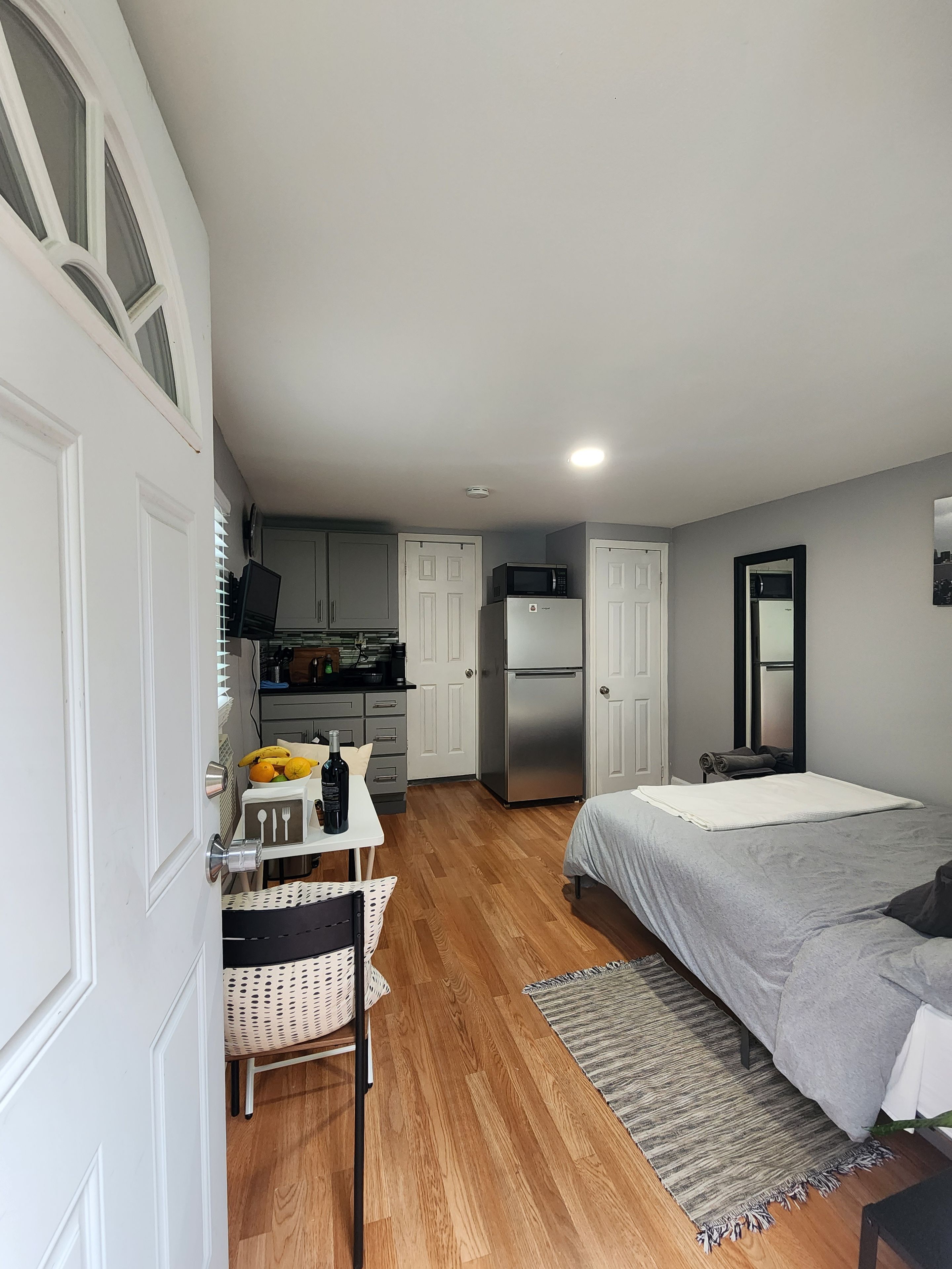 A compact bedroom with a bed, a small table with a bottle, and a chair.