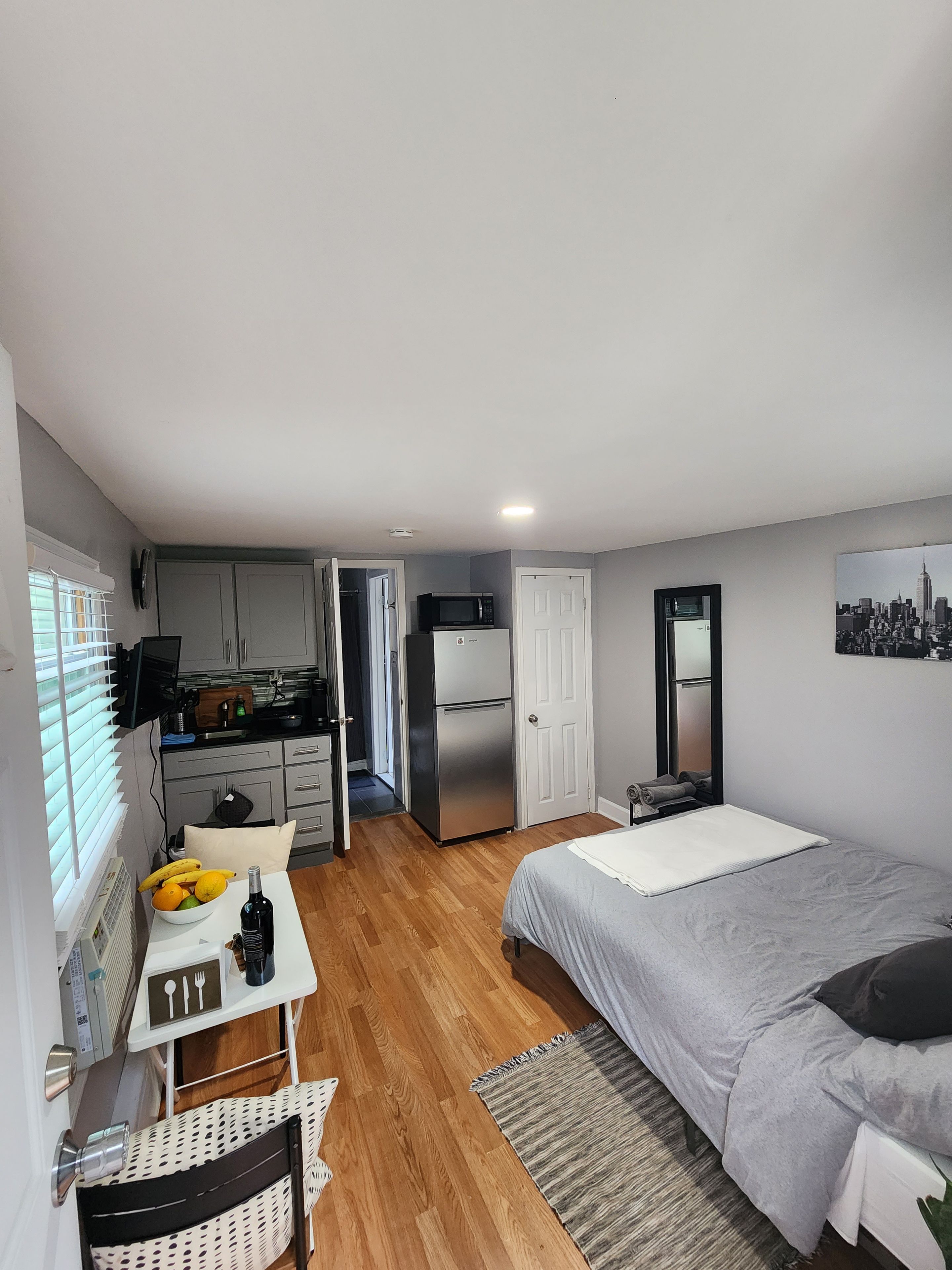 A compact room with a bed, a small table with fruits, a microwave, and a refrigerator.