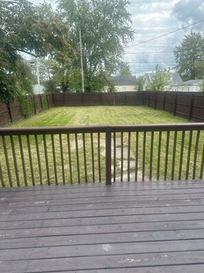 A backyard with a wooden deck, a grassy lawn, and a wooden fence.