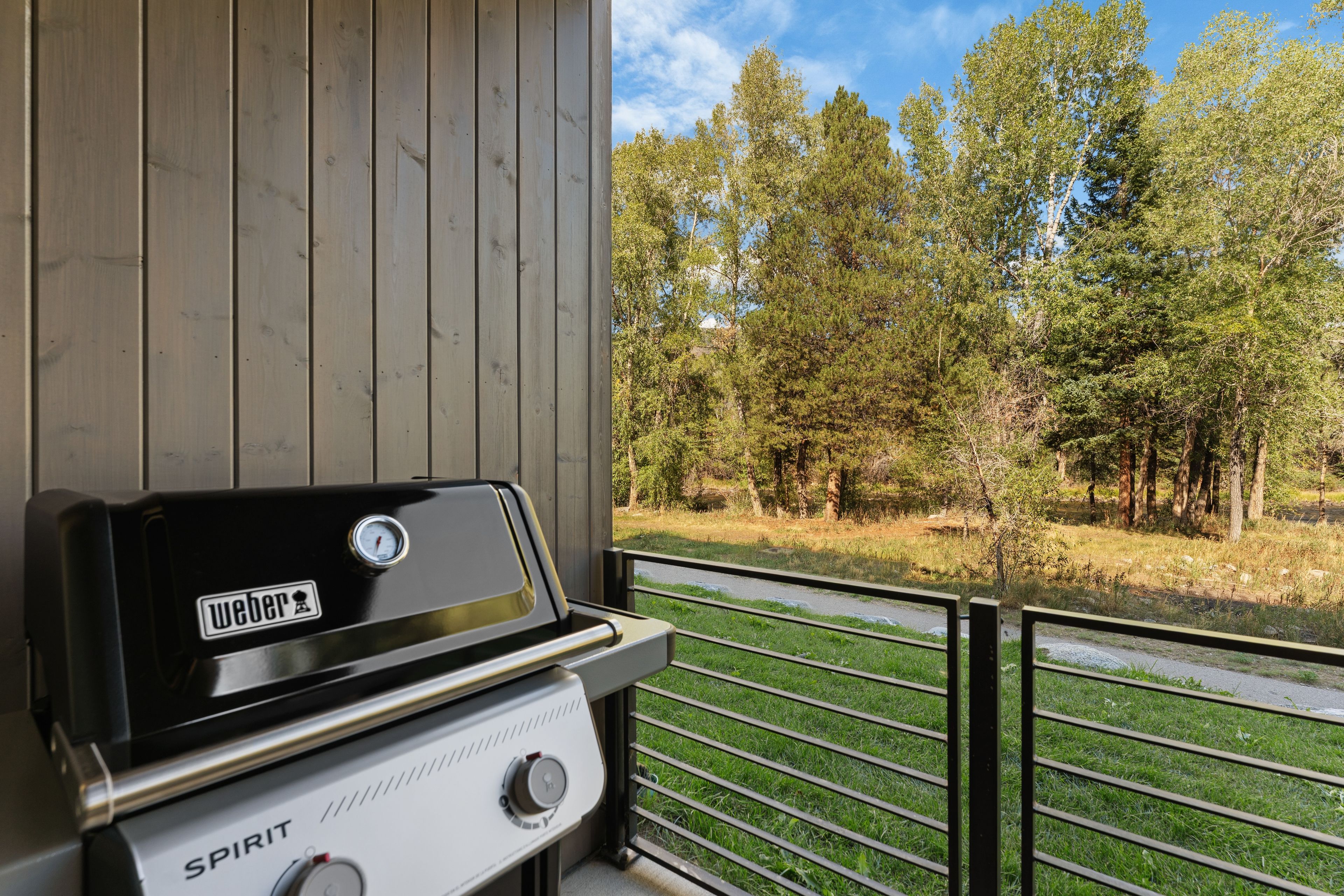 A Weber Spirit grill on a balcony with a view of a forested area.