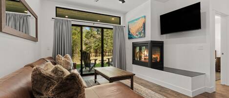A modern living room with a leather sofa, a flat-screen TV, a fireplace, and a ceiling fan.