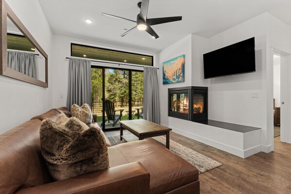 A modern living room with a leather sofa, a flat-screen TV, a fireplace, and a ceiling fan. - Cozy Blue River Getaway | Perfect Home Base for Mountain Adventures (Silverthorne)