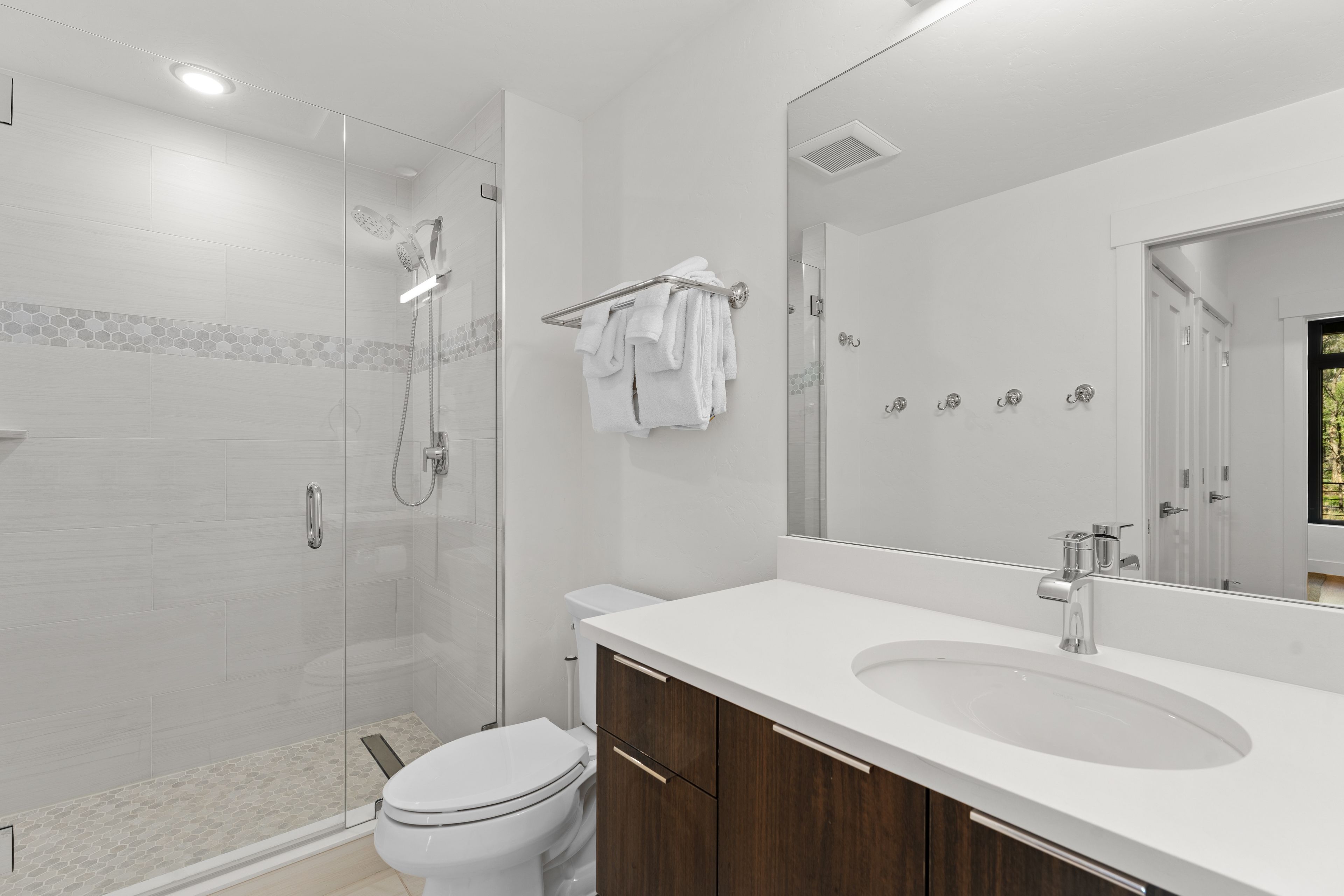 A modern bathroom with a glass shower enclosure, a white toilet, a wooden vanity, and a large mirror.