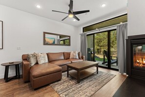 A modern living room with a sectional sofa, a coffee table, a fireplace, and a large sliding glass door leading to an outdoor area. - Cozy Blue River Getaway | Perfect Home Base for Mountain Adventures (Silverthorne)