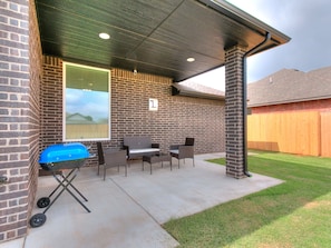 Un patio cubierto con una parrilla, muebles de exterior y una pared de ladrillo.
