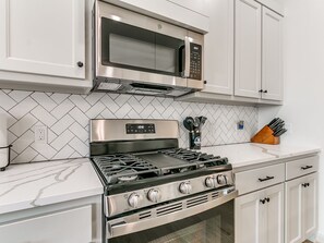 Una cocina con estufa de acero inoxidable, microondas y muebles blancos.