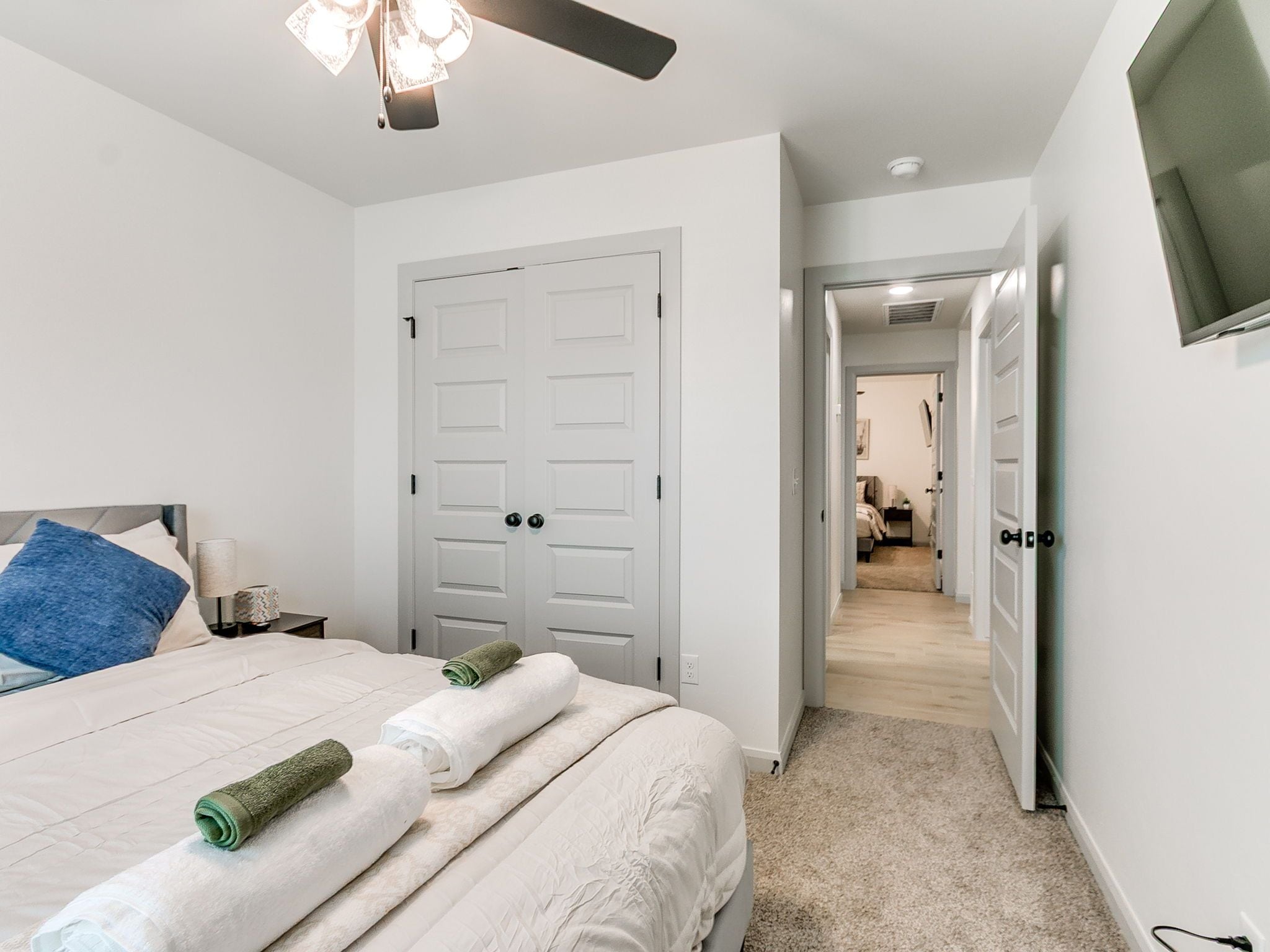 Une chambre d’hôtel avec un lit, un ventilateur de plafond, une porte et un téléviseur fixé au mur.