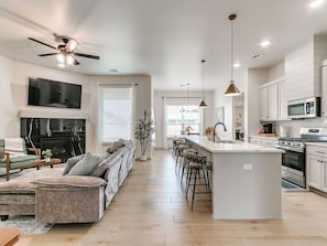 Una cocina moderna con una isla central, taburetes de bar, un comedor y una sala de estar con sofá y chimenea.