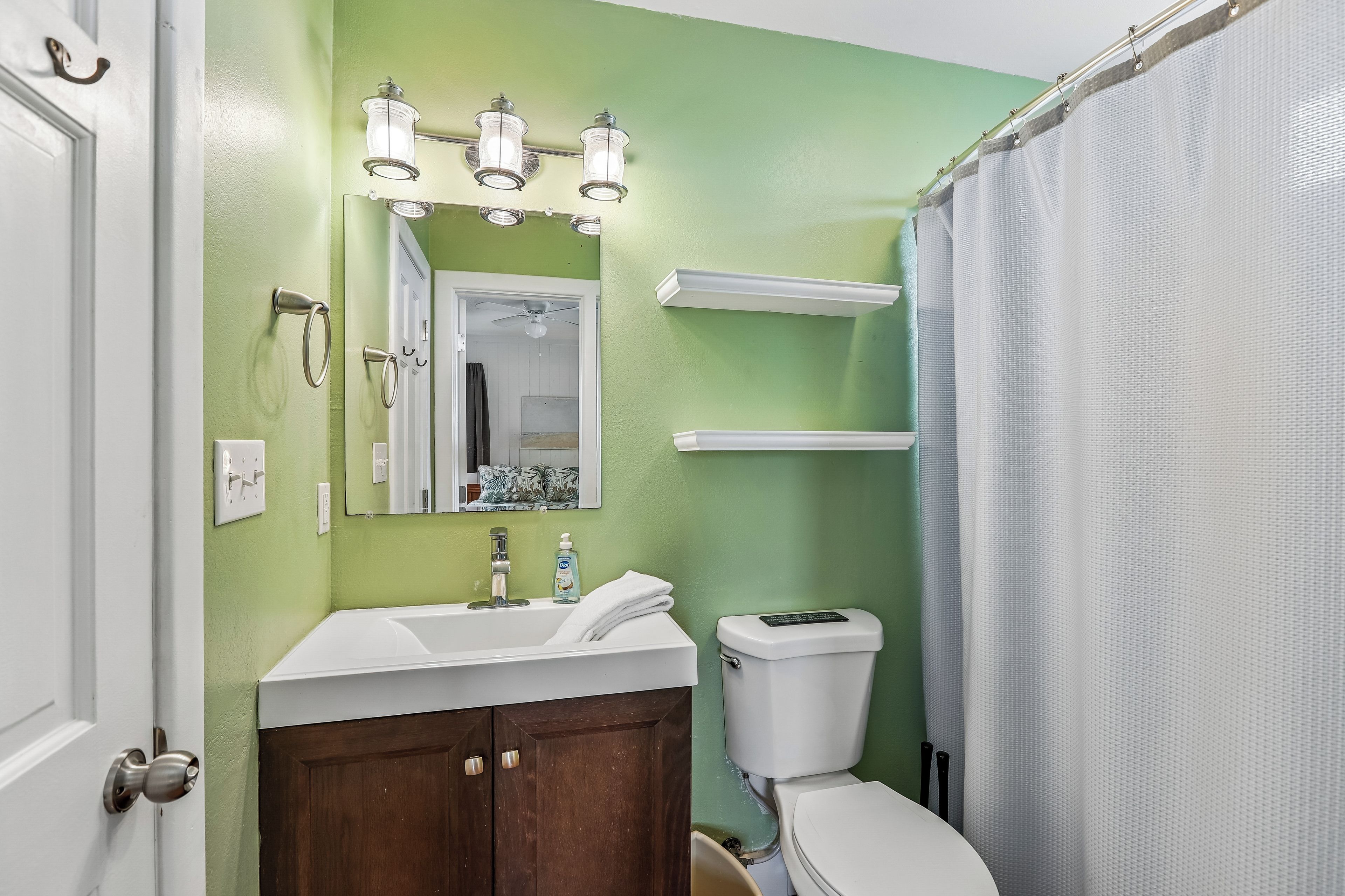 Une salle de bain avec un mur vert, un lavabo blanc, un miroir, des toilettes et un rideau de douche.