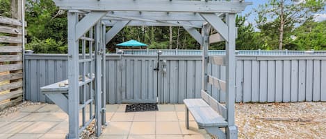 A wooden pergola with a bench and a door, surrounded by a wooden fence and a blue umbrella.
