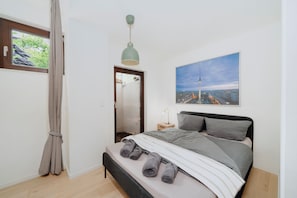 Ein Schlafzimmer mit Bett, Nachttisch, Lampe, einem Fenster mit Vorhängen und einem Stadtbild an der Wand.