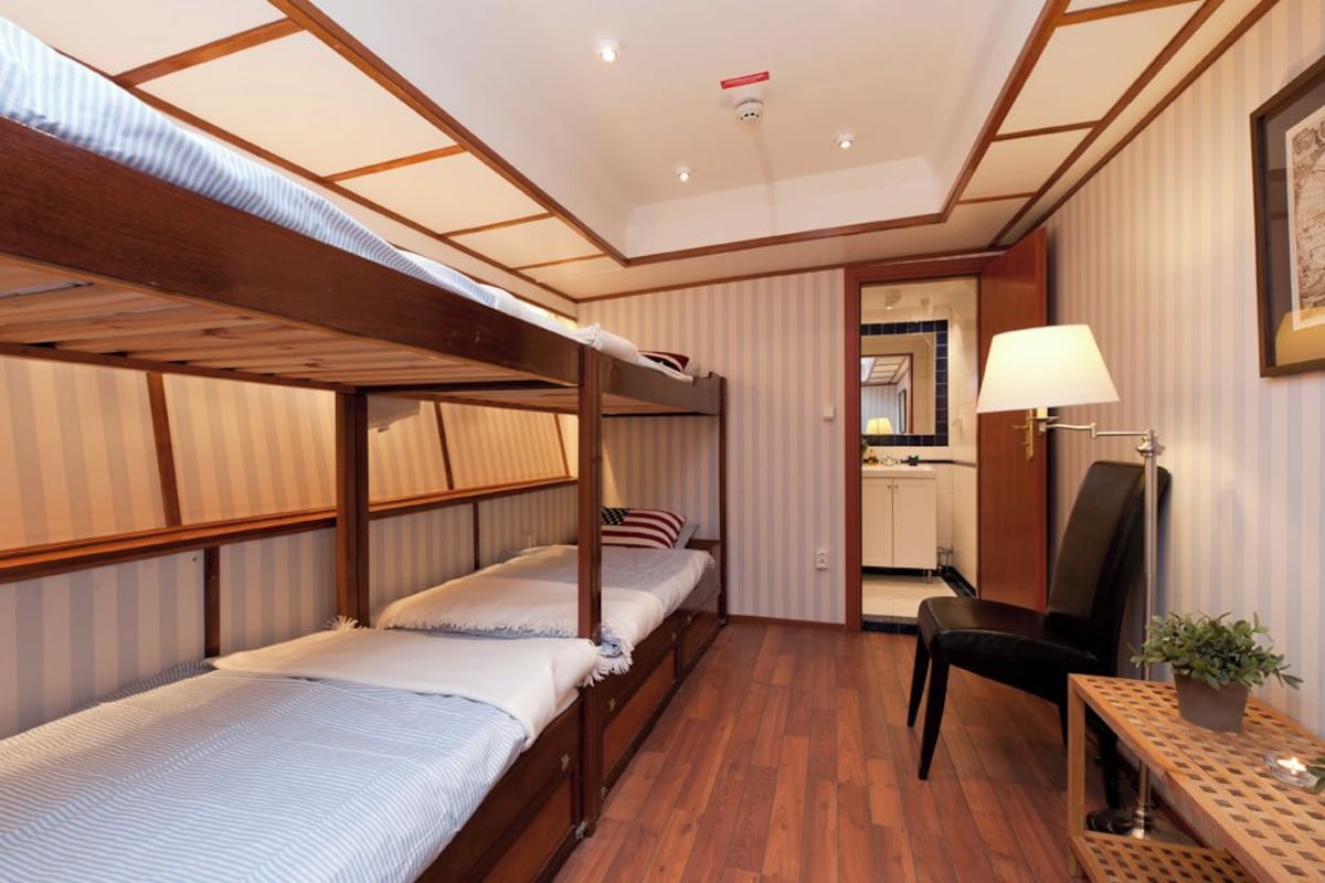 A hotel room with a bunk bed, a desk, a chair, a lamp, and a potted plant.