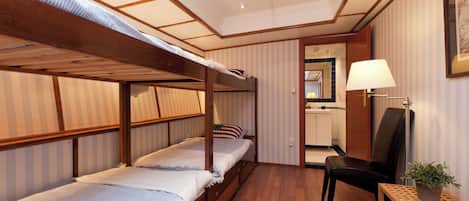 A hotel room with a bunk bed, a desk, a chair, a lamp, and a potted plant.