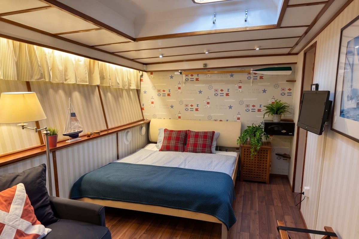 Un dormitorio con cama, mesita de noche, lámpara, televisor y ventana con cortinas.