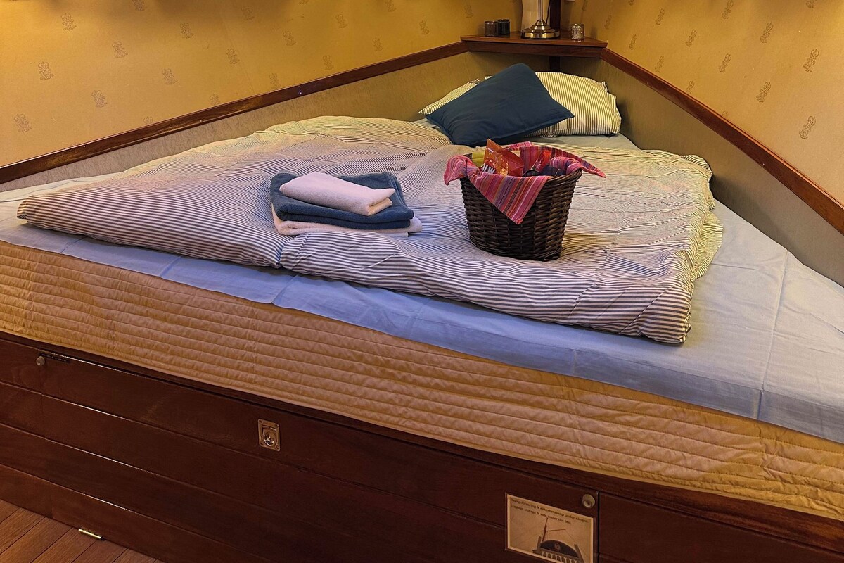 Habitación de hotel con cama, almohadas, mesita de noche, lámpara y ventana con cortinas.