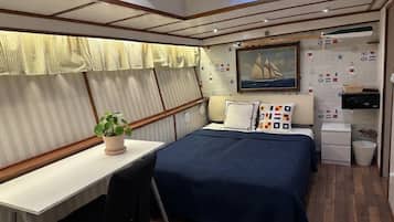 Une petite cabine comprenant un lit, un bureau et une plante en pot.
