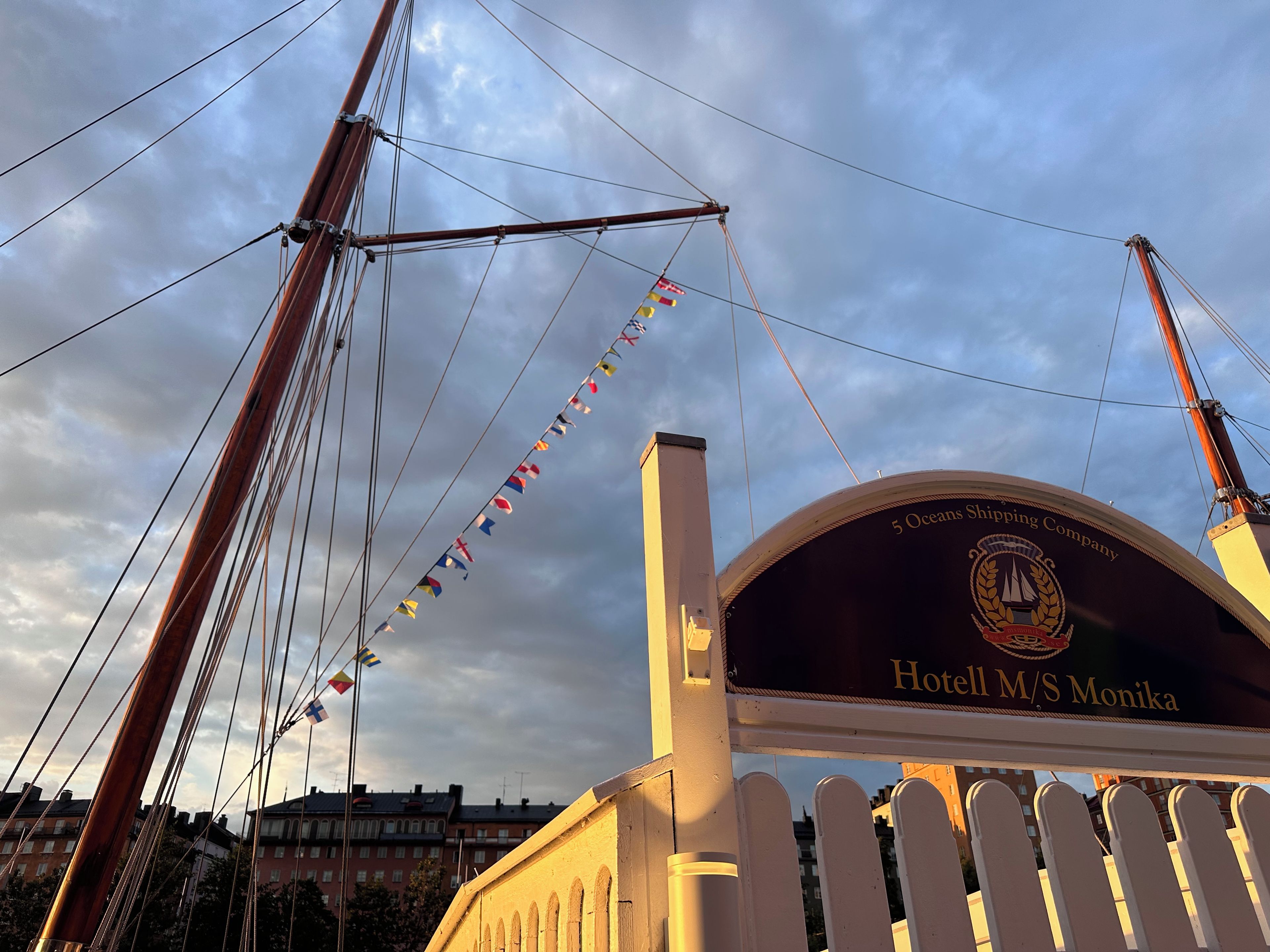 Schild für das Hotel M/S Monika, mit freier Sicht auf den Himmel und einer Reihe von Flaggen.