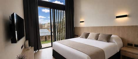 A modern hotel room with a large bed, a television, a bedside table, and a view of the outdoors.