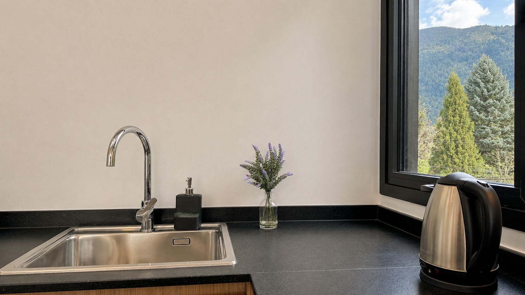 A kitchen with a stainless steel sink, a small vase with flowers, and a kettle on the counter.