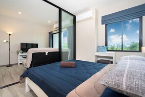 A modern bedroom with a large bed, a desk, a TV, and a view of the outdoors. - Walk to Nai Yang Beach! Stylish 7th-Floor 1BR Apt 711 - Pool, Gym, Near Airport (Tambon Sa Khu)