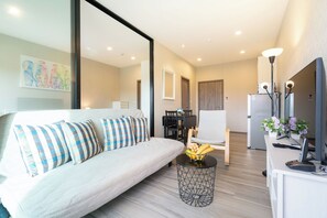 A modern living room with a sofa, a dining table, and a kitchen area with a refrigerator. - Walk to Nai Yang Beach! Stylish 7th-Floor 1BR Apt 711 - Pool, Gym, Near Airport (Tambon Sa Khu)