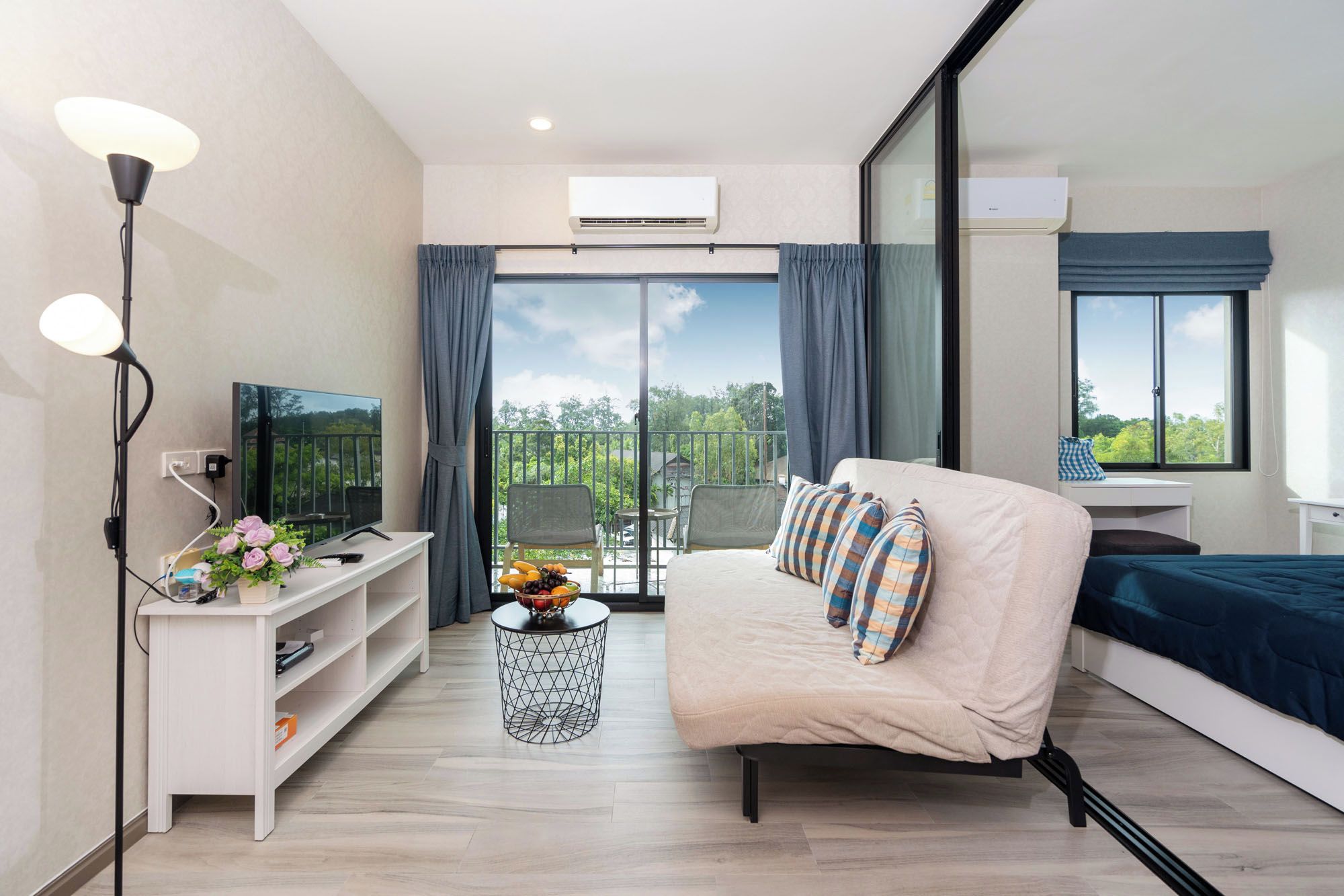 Un dormitorio moderno con sofá, televisión, una mesita con flores y un balcón con silla.