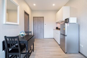 A compact kitchen with a refrigerator, a dining table with chairs, and a wooden door. - Walk to Nai Yang Beach! Stylish 7th-Floor 1BR Apt 711 - Pool, Gym, Near Airport (Tambon Sa Khu)