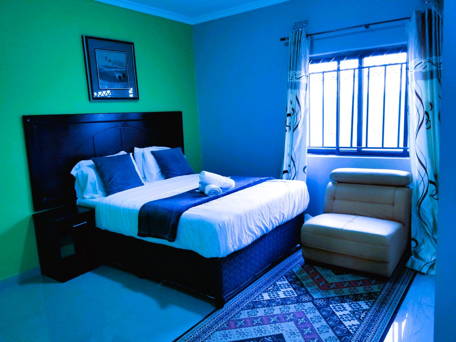 A bedroom with a bed, a chair, a window with curtains, and a patterned rug.