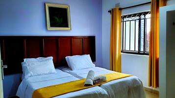 Une chambre d’hôtel avec deux lits, une tête de lit en bois, un tableau encadré au mur et une fenêtre avec des rideaux.
