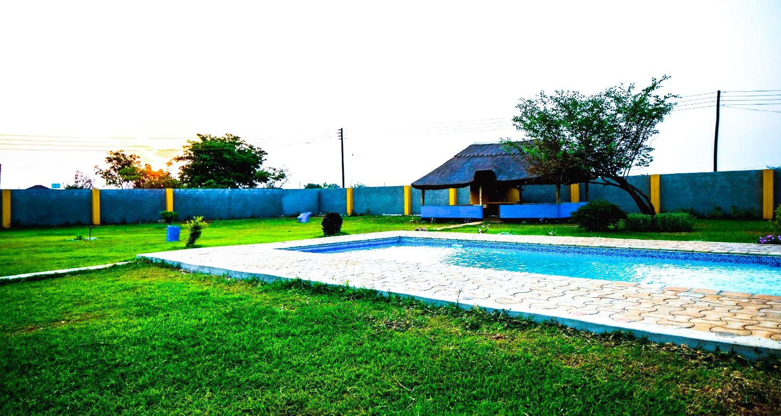 A swimming pool with a tiled deck, surrounded by a grassy lawn and a low blue wall.