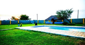A swimming pool with a tiled deck, surrounded by a grassy lawn and a low blue wall.