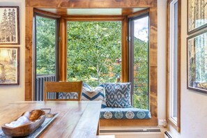 A room with a wooden table, a bench with patterned cushions, and a view of greenery through large windows. - Timber Falls - Top Floor Views & Steps to Bus (Vail)