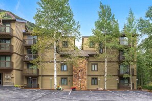 A multi-story building with balconies, a stone facade, and a parking lot. - Timber Falls - Top Floor Views & Steps to Bus (Vail)