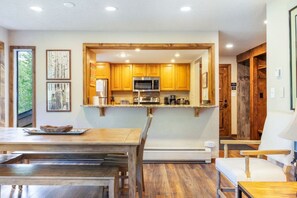 A modern kitchen with wooden cabinets, a microwave, and a dining area with a table and chairs. - Timber Falls - Top Floor Views & Steps to Bus (Vail)