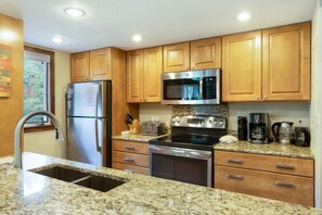 A kitchen with wooden cabinets, stainless steel appliances, granite countertops, and a window. - Timber Falls - Top Floor Views & Steps to Bus (Vail)