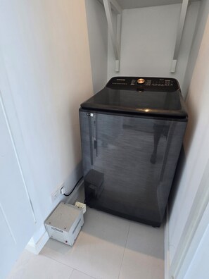 Une machine à laver compacte, de couleur noire, est placée dans un coin d’une pièce aux murs blancs et au sol carrelé.