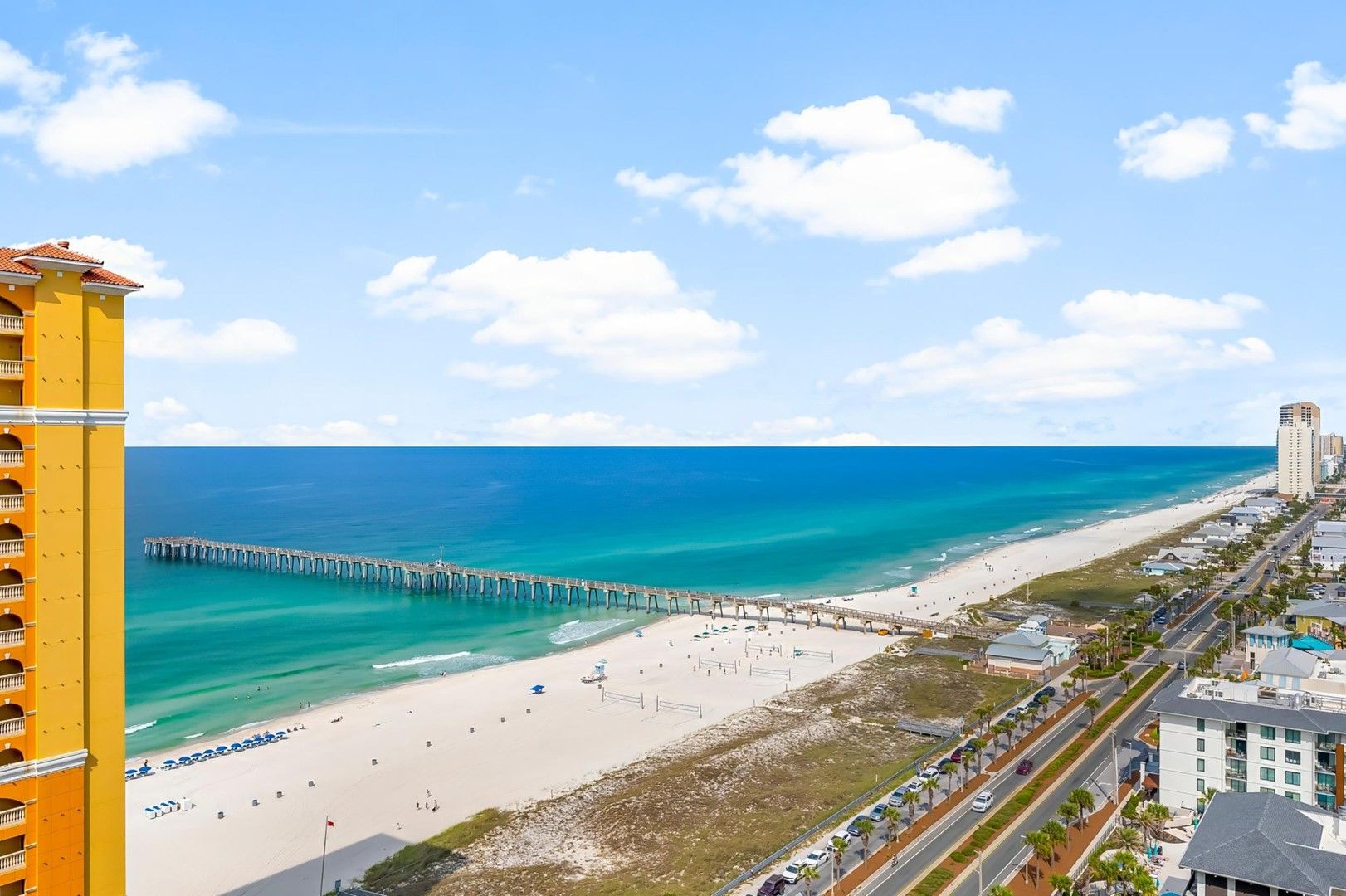 A coastal cityscape with a beach, a pier, and a tall building.