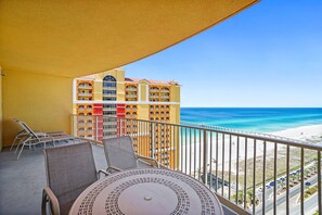 A balcony with a table and chairs, overlooking a beach and a hotel building. - Steps to The Beach • Resort Pools • Pier Park (Panama City Beach)