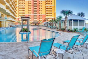 Un espace piscine d’hôtel comprenant une grande piscine, des chaises longues et un bâtiment avec des balcons en arrière-plan.