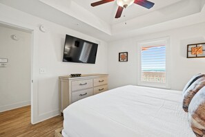 A bedroom with a bed, a dresser, a television, a ceiling fan, and a window with a view. - Steps to The Beach • Resort Pools • Pier Park (Panama City Beach)