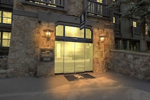 Ingresso di un hotel con facciata in pietra, una porta in vetro e due lanterne a parete.
