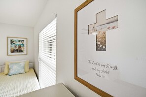 Une chambre à coucher avec un lit, un cadre contenant une citation religieuse et une fenêtre avec des stores.