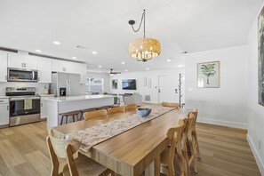 Una cocina moderna con armarios blancos, electrodomésticos de acero inoxidable y una mesa de comedor de madera con sillas.