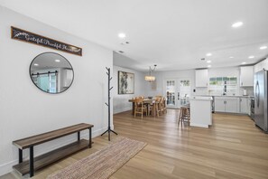 Una cocina moderna con armarios blancos, un refrigerador de acero inoxidable y un comedor con sillas y una mesa de madera.