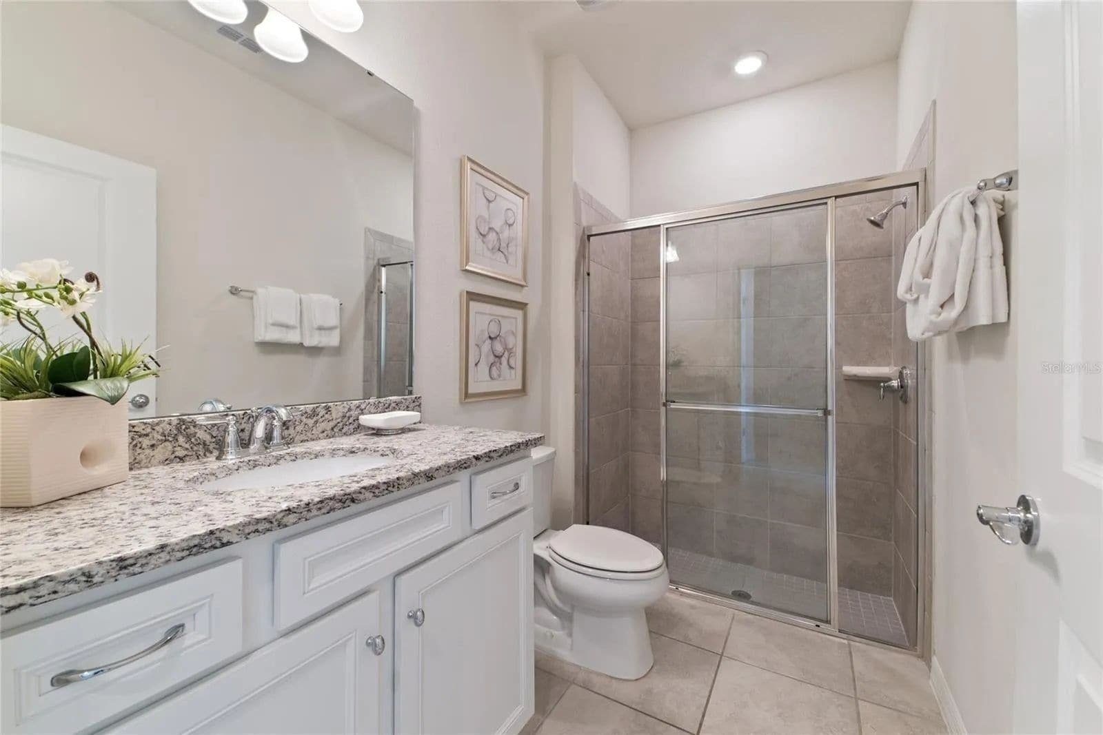 A modern bathroom with a granite countertop, white cabinetry, a glass-enclosed shower, and a toilet.